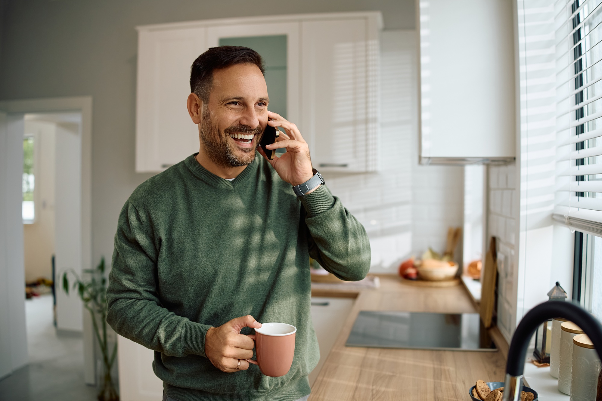 Happy man talking on smart phone in the kitchen.
