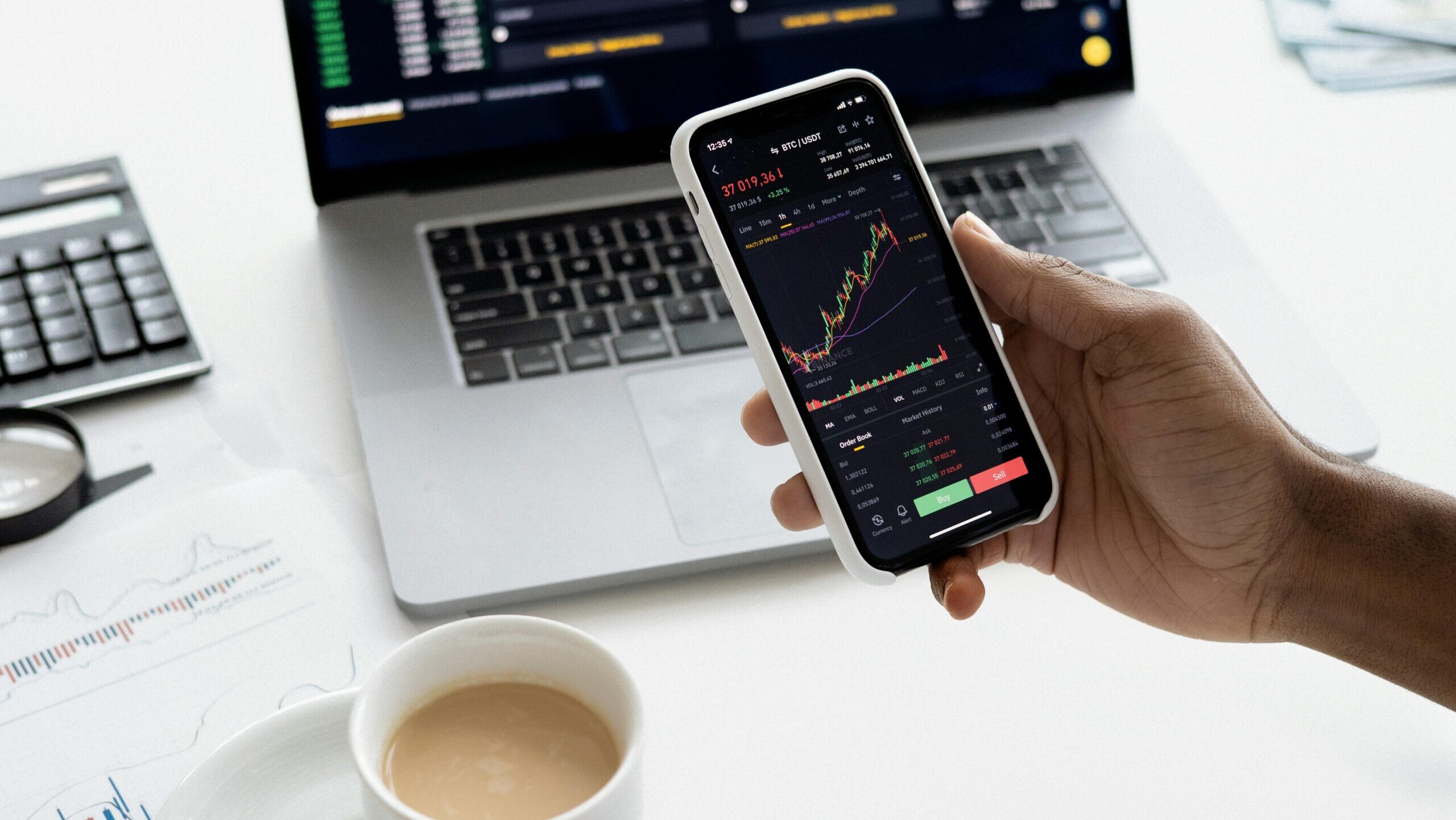 Trader analizando gráficos de trading en el móvil frente a su laptop, comparando estrategias de Intradía vs Swing Trading en Prop Firm.